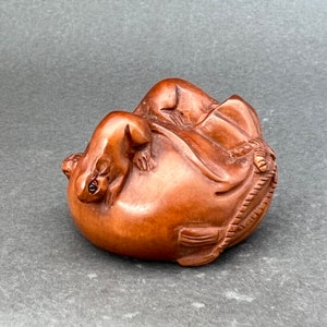 Puede incluir: Una escultura de madera tallada a mano de dos ratones sobre una calabaza. Los ratones están intrincadamente detallados y tienen rasgos realistas. La calabaza es de color marrón natural y tiene una superficie lisa.