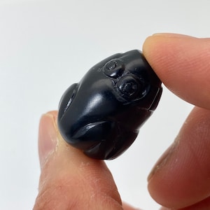 May include: A small, black, carved frog figurine with detailed eyes.
