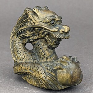 May include: A detailed, intricately carved wooden dragon figurine with a golden finish. The dragon is curled up with its head turned to the side, and its scales are visible.