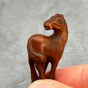 May include: A small, intricately carved wooden horse figurine. The horse is brown and has a detailed mane and tail. The figurine is standing on its hind legs and has its head turned to the side.