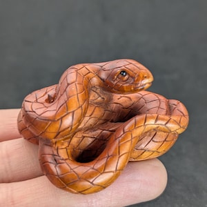 May include: A hand-carved wooden snake figurine. The snake is coiled and has a detailed, textured surface. The snake is brown and has a black eye.