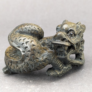 May include: A detailed wood carving of a dragon in a curled up position. The dragon is a dark brown color and has intricate details carved into its scales and claws.