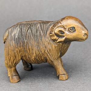 May include: A hand-carved wooden sculpture of a brown sheep with detailed features, including horns and a textured wool coat.