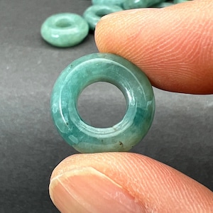 May include: A green jade donut bead with a smooth, polished surface. The bead is approximately 1 inch in diameter.