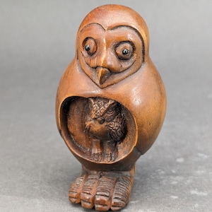 May include: A hand-carved wooden owl figurine with intricate details. The owl is depicted with its wings folded around its body, and its eyes are wide open. The owl is painted in shades of brown and has a natural wood finish.