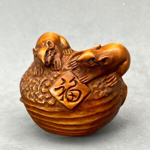 May include: A wooden carving of two mice on a walnut shell. The mice are carved in a realistic style and the walnut shell is detailed with wood grain. The carving is a traditional Japanese folk art form.