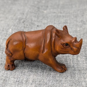 May include: A small, intricately carved wooden rhinoceros figurine. The figurine is brown and has a detailed face with black eyes.