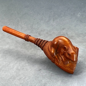 Puede incluir: Una pipa de madera con una rata tallada en el extremo. La pipa es marrón y tiene una boquilla larga y fina.