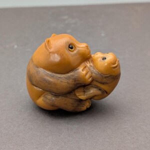May include: A carved wooden sculpture of two bears, one embracing the other. The bears are a light brown color with darker brown stripes. The sculpture is detailed with visible eyes and a smooth finish. The bears are in a hugging pose.