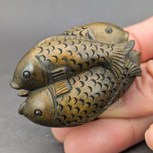 Peut inclure: Une main tient une petite sculpture en bois de trois poissons finement sculptés. Les poissons sont bruns et ont des écailles et des nageoires détaillées.