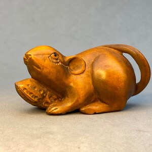 May include: A small, intricately carved wooden sculpture of a brown rat holding a nut in its paws. The rat is lying on its side with its tail curled around its body.