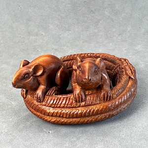 Puede incluir: Dos ratones de madera tallados intrincadamente anidados en una serpiente enroscada, una escultura netsuke japonesa tradicional.