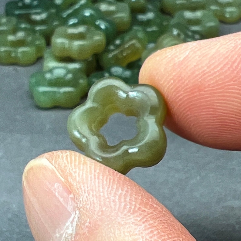 May include: A close-up of a green flower-shaped bead with a hole in the center. The bead is made of a translucent material and has a glossy finish.
