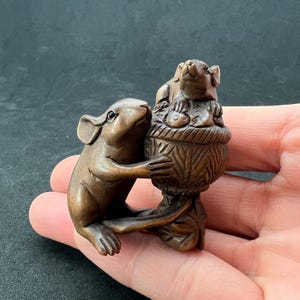 Puede incluir: Una escultura de madera tallada a mano de dos ratones. El ratón más grande sostiene una cesta llena de fruta. El ratón más pequeño está sentado encima de la cesta.