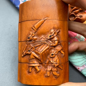 May include: A wooden box with a carved design of four mice pulling a cart. The box is made of light brown wood and has a smooth finish.