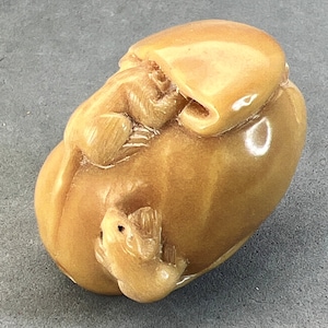 May include: A small, intricately carved ivory sculpture of a man with a hat, holding a small animal in his hand. The sculpture is a light brown color and has a smooth, polished finish.