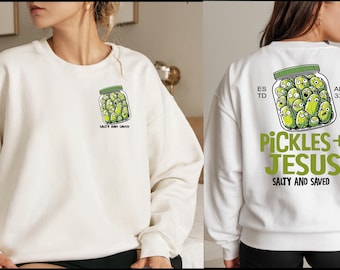 May include: Off-white sweatshirt featuring a jar of cartoon pickles with the text "Salty and Saved" on the front. The back displays a larger graphic of pickles in a jar with "Pickles + Jesus" and "Salty and Saved".