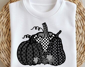 May include: White sweatshirt with a black and grey pumpkin design. The pumpkins have checkered and plaid patterns, with floral accents at the base. The design is centered on the front of the sweatshirt.