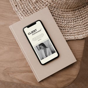 May include: A smartphone displaying a client testimonial page with the text CLIENT testimonial, a short paragraph, and a black and white photograph of a person in a blazer, resting on a beige notebook next to a woven straw hat.