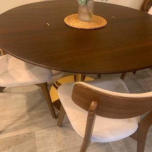 May include: A round wooden dining table with a gold base and four chairs. The table has a dark wood finish and the chairs have light beige upholstery.