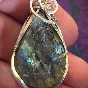 May include: A silver wire wrapped pendant featuring a teardrop-shaped labradorite gemstone with iridescent blue and green hues.