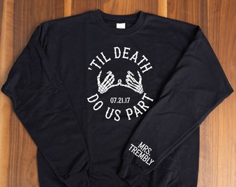 May include: Black long-sleeved sweatshirt with white text that reads "'Til Death Do Us Part" with a skeleton hand design and the date 07.21.17. The right sleeve has the text "Mrs. Trembly" in white.