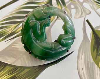 May include: A green jade ring with a carved design of a lizard or dragon. The ring is set in silver and has a polished finish.