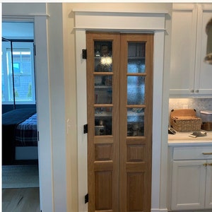 May include: A set of two wooden cabinet doors with glass panels. The doors have a light brown stain and are framed with white trim. The glass panels have a textured pattern and are divided into four sections.