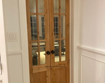 Może przedstawiać: Dwu skrzydłowe drzwi francuskie z matowymi szklanymi panelami i drewnianą ramą. Drzwi mają czarne gałki i tabliczkę z napisem "Northern Edge Woodshop Co."