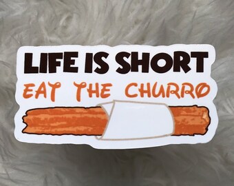 May include: White sticker with black text that reads "Life is short eat the churro". A brown and orange churro is wrapped in white paper.