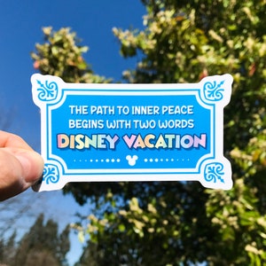 May include: A blue sticker with white border and ornate corners. The sticker says "The path to inner peace begins with two words: Disney Vacation". The text is in a rainbow font with a Mickey Mouse silhouette in the center.