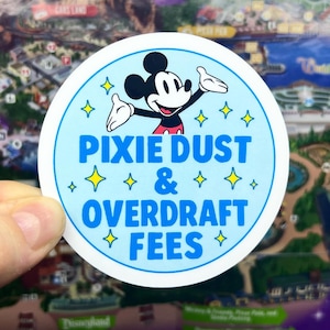 May include: A round sticker featuring Mickey Mouse with the text "PIXIE DUST & OVERDRAFT FEES". The sticker has a light blue background with yellow star accents and a white border. Mickey Mouse is in the center.