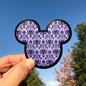 May include: Purple and black Mickey Mouse head sticker with a repeating pattern of a haunted house design.