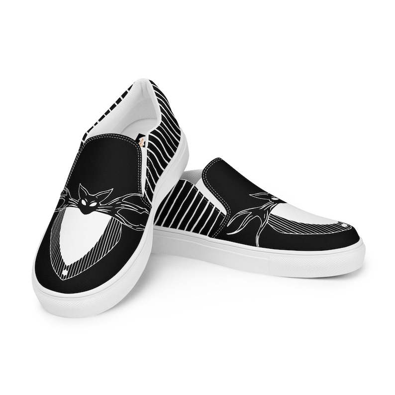 Puede incluir: Zapatillas de lona negras y blancas de deslizamiento con un patr&oacute;n a rayas y un gr&aacute;fico de la cara de Jack Skellington de Pesadilla antes de Navidad.