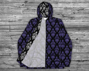 May include: A black hooded jacket with a purple and white repeating pattern. The jacket is unzipped, showing the inside lining. The lining is a light gray color with a faint purple pattern.