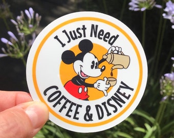 May include: A round sticker with a yellow border and a white background. The sticker features a cartoon image of Mickey Mouse pouring coffee from a pot into a cup. The text "I Just Need Coffee & Disney" is written in a black circle around Mickey Mouse.