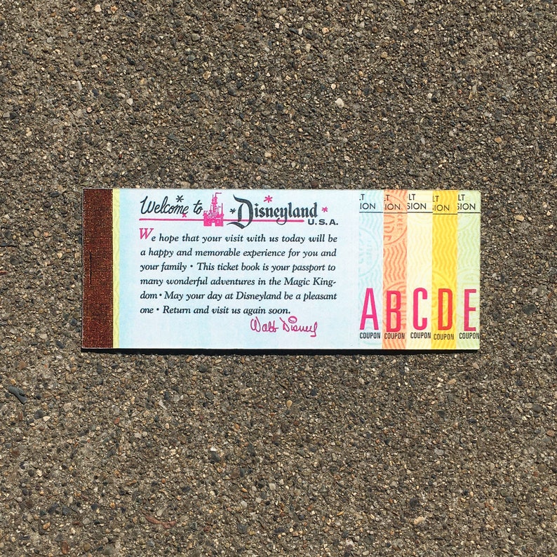 May include: A vintage Disneyland ticket book with a pink and yellow color scheme. The cover features the Disneyland castle logo and the text "Welcome to Disneyland U.S.A.". The inside of the book has a message from Walt Disney, "We hope that your visit with us today will be a happy and memorable experience for you and your family. This ticket book is your passport to many wonderful adventures in the Magic Kingdom. May your day at Disneyland be a pleasant one. Return and visit us again soon. Walt Disney."