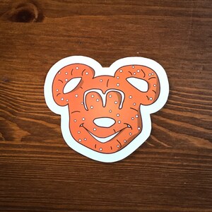 May include: A brown pretzel shaped like Mickey Mouse with white sprinkles.