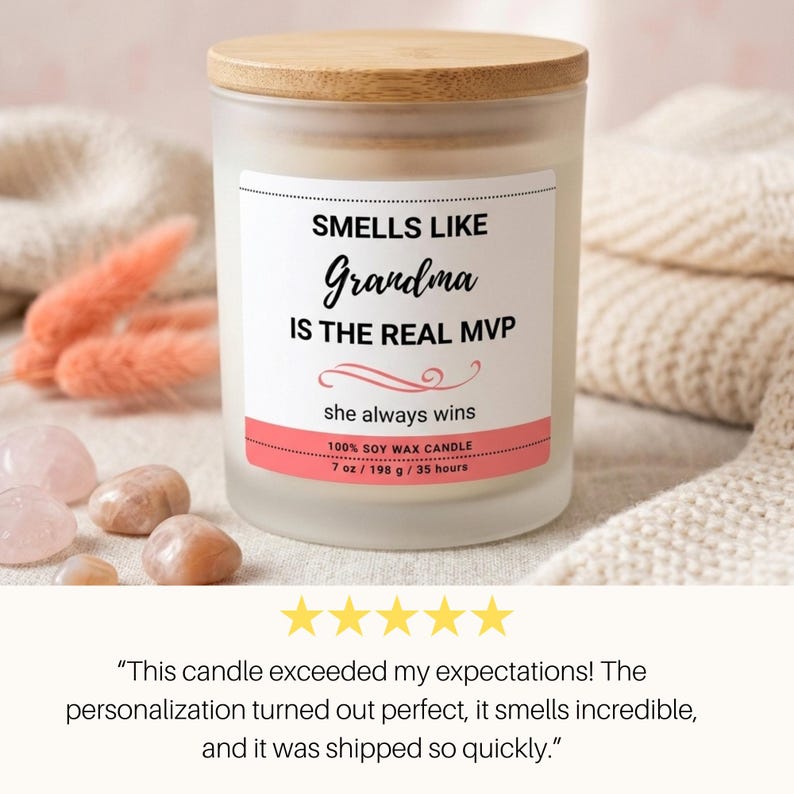 K&ouml;nnte beinhalten: Duftkerze in einem mattierten Glas mit Holzdeckel. Das Etikett lautet "SMELLS LIKE Grandma IS THE REAL MVP" mit "she always wins" darunter. Die Kerze hat 198 g und brennt 35 Stunden. Rosa Akzente und Steine sind sichtbar.