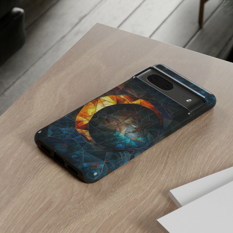 May include: A black phone case with a geometric design featuring a circle of blue, orange, and yellow mosaic tiles.