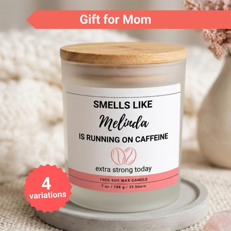 K&ouml;nnte beinhalten: Eine Kerze aus mattiertem Glas mit einem Holzdeckel. Auf dem Etikett steht "Smells Like Melinda Is Running on Caffeine". Die Kerze ist 198 g und besteht aus 100 % Sojawachs. Der Text "Gift for Mom" steht dar&uuml;ber.