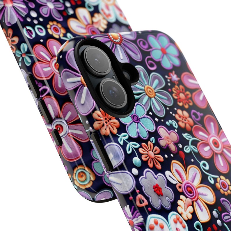 Op de afbeelding: Een close-up van twee telefoonhoesjes met een bloemenpatroon. De hoesjes zijn donkerblauw met een herhalend patroon van kleurrijke bloemen in roze, paarse, oranje en blauwe tinten. De bloemen hebben een verhoogde, getextureerde uitstraling.