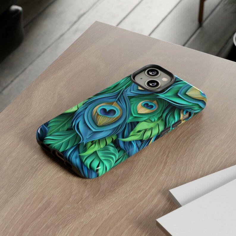 May include: A phone case with a peacock feather design. The case is black with a green, blue, and gold peacock feather pattern.