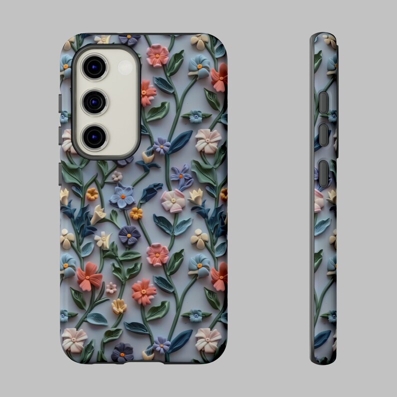 Op de afbeelding: Een telefoonhoesje met een bloemenpatroon. Het hoesje is gemaakt van hard plastic en heeft een reli&euml;f bloemenpatroon. De bloemen zijn in tinten roze, blauw en groen. Het hoesje is ontworpen om te passen op een smartphone met een camerabult.