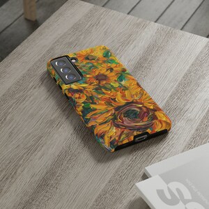 May include: A phone case featuring a colourful sunflower painting design. The case is black and has a cut-out for the camera lens.