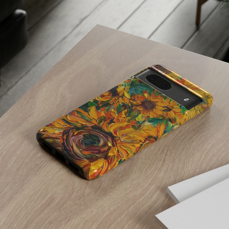 May include: A black phone case featuring a colourful sunflower design. The case has a raised camera bump and a cut-out for the phone's charging port.