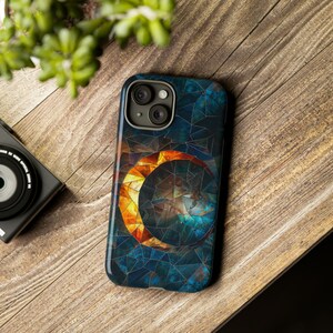 May include: A phone case with a mosaic design featuring a crescent moon with a sun-like pattern inside. The case is blue, green, and orange.