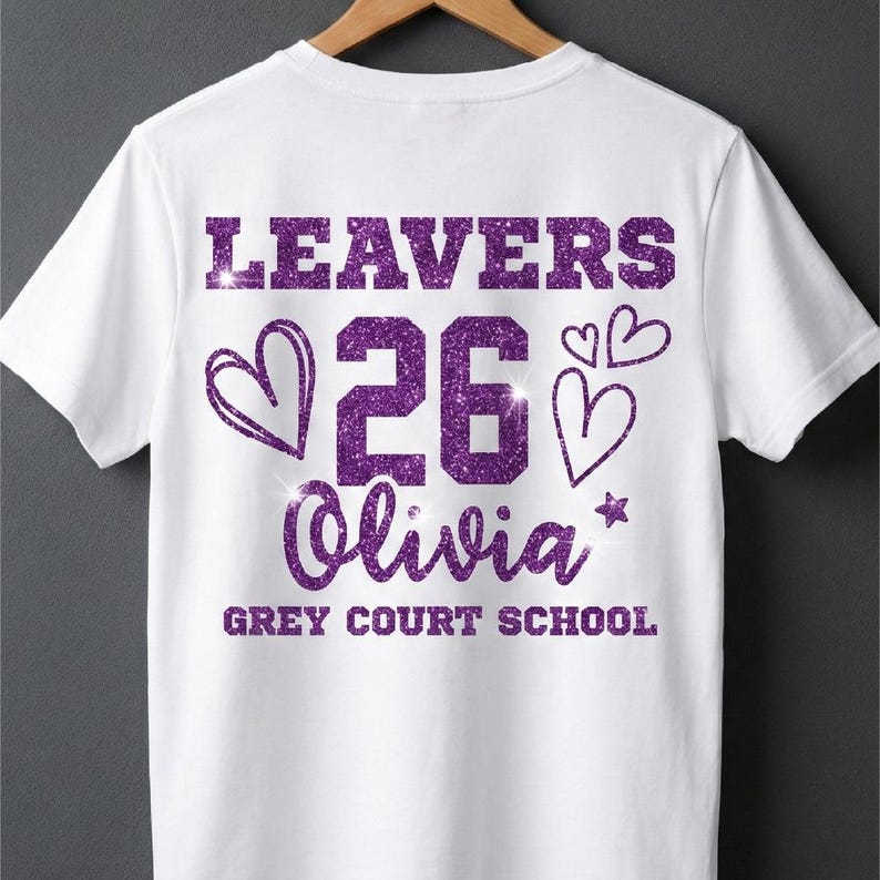Peut inclure: T-shirt blanc avec texte paillet&eacute; violet &laquo;&nbsp;LEAVERS 26 Olivia&nbsp;&raquo; avec des graphiques de c&oelig;ur et d'&eacute;toile. En dessous du nom se trouve &laquo;&nbsp;GREY COURT SCHOOL&nbsp;&raquo;. Le t-shirt est suspendu &agrave; un cintre en bois.