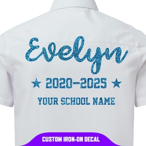 Può includere: Camicia bianca con bottoni con un design glitterato blu. Il design include il nome "Evelyn", gli anni "2020-2025" tra due stelle e il testo "YOUR SCHOOL NAME". La parte inferiore della camicia riporta la scritta "CUSTOM IRON-ON DECAL".