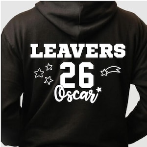 Peut inclure: Un sweat &agrave; capuche noir avec l'inscription blanche "LEAVERS 26 Oscar", accompagn&eacute;e d'&eacute;toiles et d'une &eacute;toile filante. V&ecirc;tement d&eacute;contract&eacute;, id&eacute;al pour un &eacute;v&eacute;nement de fin d'&eacute;tudes.